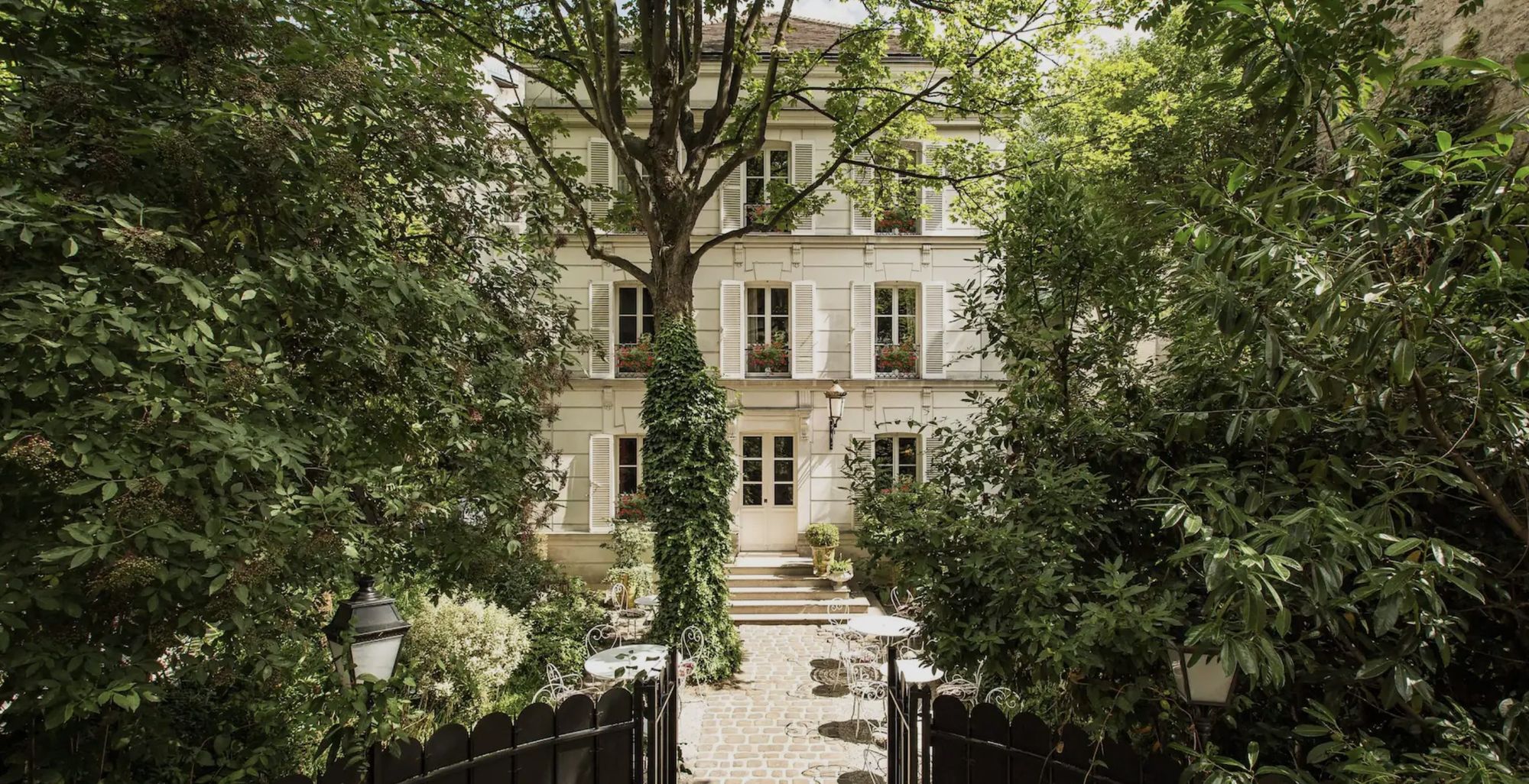 Cream-coloured townhouse with shuttered windows, seen through a green garden in Montmartre